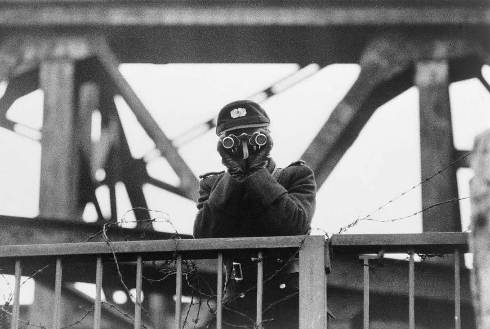 East German VOPO, a quasi-military border policeman using binoculars, standing guard on one of the bridges linking East and West Berlin, in 1961.