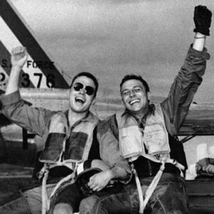 Three happy fliers of the 18th Fighter Bomber wing let the world know how they feels as they returned from a combat mission over North Korea to learn of the armistice signing on July 29, 1953. Left to right are: 2nd Lt. John Putty, Dallas, Tex.; 1st Lt. James A. Boucek, Ottawa, Kansas,: and 1st Lt. Richard D. Westcott, Houston, Tex., waving from the back seat of the jeep.