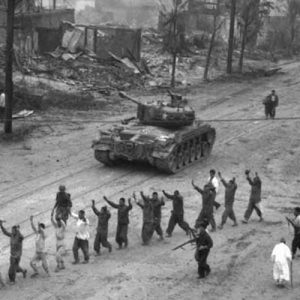 A U.S. Marine tank follows a line of prisoners of war down a village street. September 26, 1950.